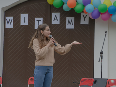 Dziewczyna z mikrofonem stojąca przed budynkiem.