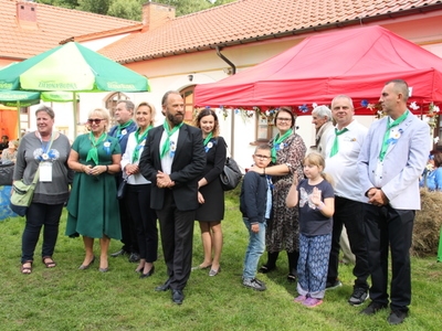Grupa elegancko ubranych osób stojąca na tle czerwonego namiotu.