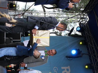 Zdjęcie dziecka odbierającego duże pudło od elegancko ubranego mężczyzny na scenie.