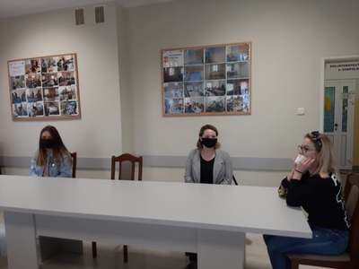 Na zdjęciu znajdują się trzy osoby siedzące przy stole. Wszyscy mają na twarzy maseczki.