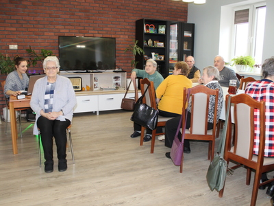 Fotografia przedstawia starszą kobietę siedzącą tyłem do stołu na którym stoi laptop. Komputer obsługuje instruktorka zajęć, która włącza dźwięki do rozpoznawania za pomocą zmysłu słuchu.