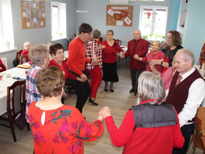 Fotografia przedstawia seniorów i opiekunów tańczących w kółku.