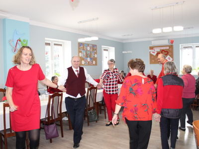 Fotografia przedstawia seniorów i opiekunów tańczących w wesołym pociągu.