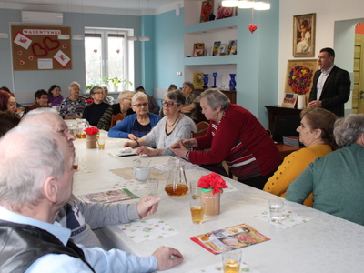 Zdjęcie wykonane w sali głównej Domu Dziennego Pobytu Senior+ w Sompolnie podczas wykładu na temat rehabilitacji. Na zdjęciu widać seniorów siedzących przy stole i słuchających prelekcji.