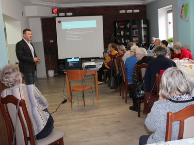 Na fotografii widać doktora Tomasza Pieńkowskiego tłumaczącego seniorom zagadnienia dotyczące rehabilitacji.
