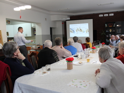 Fotografia przedstawia doktora Tomasza Pieńkowskiego prezentującego seniorom slajdy ze zdjęciami zmian zwyrodnieniowych.