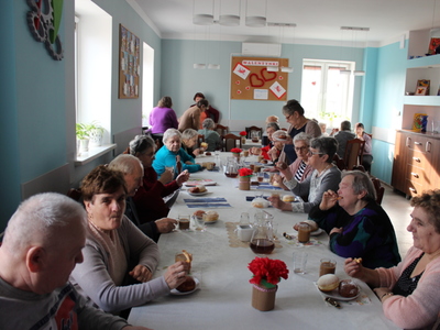 Na zdjęciu widać seniorów siedzących przy stołach i jedzących słodkości z okazji tłustego czwartku.