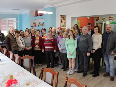 Fotografia grupowa wykonana w sali głównej domu dziennego pobytu senior+ w Sompolnie. Widać na niej grupę seniorów oraz gości przybyłych na „Zabawną lekcję języka angielskiego”.
