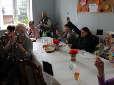 Zdjęcie przedstawia grupę seniorów biorących udział w zabawie tematycznej podczas zabawnej lekcji języka angielskiego.
