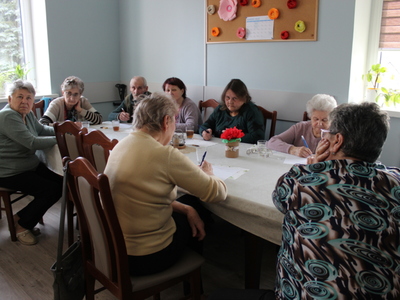 Fotografia przedstawia seniorów siedzących przy stole podczas rozwiązywania quizu.