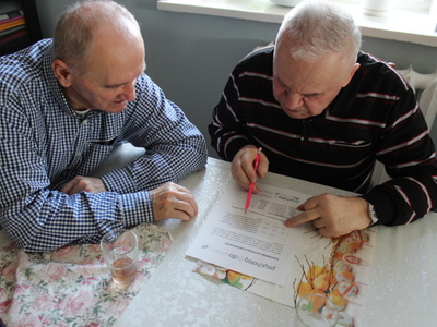 Zdjęcie przedstawia dwóch seniorów siedzących przy stole, rozwiązujących ćwiczenia na pamięć i koncentrację.