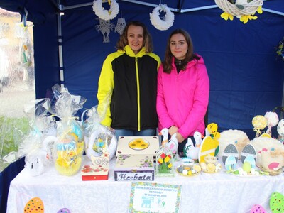 Zdjęcie wykonane podczas Sompoleńskiego Kiermaszu Wielkanocnego. Przedstawia stoisko Domu Dziennego Pobytu Senior+ w Sompolnie. W tle dwie kobiety – pracownice DDP.