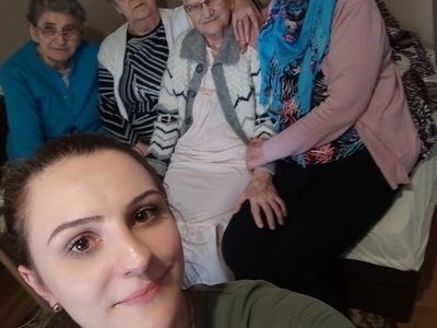 Na zdjęciu cztery seniorki siedzące na kanapie u jednej z odwiedzanych koleżanek oraz fizjoterapeutka z Domu Dziennego Pobytu Senior+ w Sompolnie.