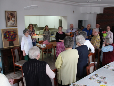 Zdjęcie wykonane w sali głównej Domu Dziennego Pobytu Senior+ w Sompolnie. Przedstawia seniorów i gości zebranych na jubileuszu 90 urodzin jednej z uczestniczek DDP