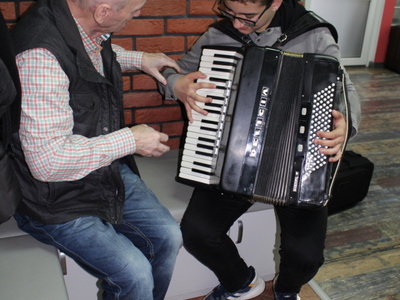 Na zdjęciu uczestnik DDP uczący grać na akordeonie jednego z przybyłych uczniów.