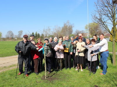 Zdjęcie przedstawia wszystkich uczestników spotkania przy urzędzie gminy, którzy dumnie i z uśmiechami na twarzach wskazują na swoje drzewo.