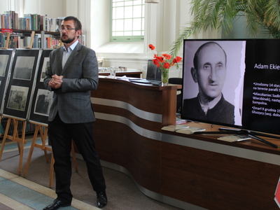 Zdjęcie przedstawia dr Krzysztofa Żabierka. Po lewej stronie sztalugi ze zdjęciami Monte Cassino, a po prawej stronie zdjęcie Adama Ekierta – żołnierza walczącego pod Monte Cassino.