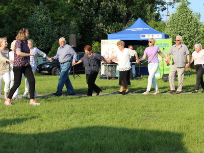 Seniorzy i pracownicy MGOPS tańczący na trawie.