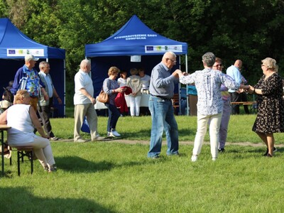 Seniorzy tańczący w kółku na trawie.