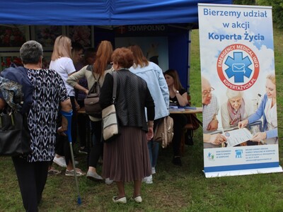 Zdjęcie przedstawia seniorów przy namiocie z informacjami na temat Koperty Życia.