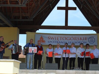 Na zdjęciu seniorzy na scenie plenerowej w Świętej Górze. Po lewej stronie dyrektor mgops grający na gitarze, uczestnik ddp grający na akordeonie oraz instruktor muzykoterapii grający na gitarze.