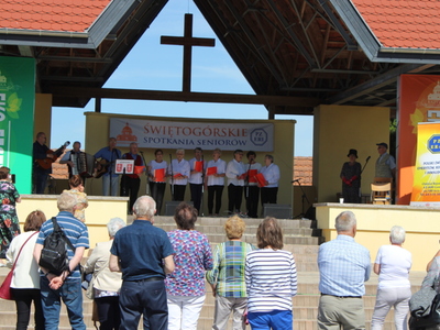 Zdjęcie przedstawia seniorów na scenie plenerowej w Świętej Górze oraz publiczność oglądającą ich występ.