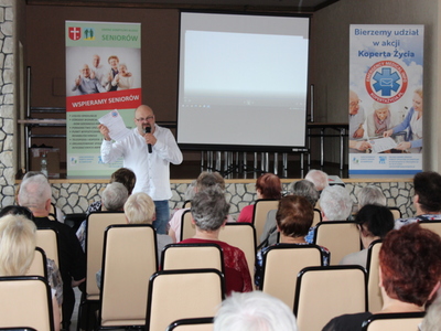 3)	Zdjęcie przedstawia dyrektora MGOPS w Sompolnie prezentującego kartę informacyjną. Przed nim na krzesłach siedzą osoby zainteresowane