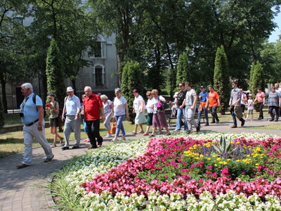 8)	Na zdjęciu przewodnik prowadzący wycieczkę. Z prawej strony kolorowy dywan kwiatowy.