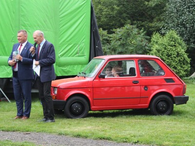 14)	Na zdjęciu Pan Roman Bednarek oraz Andrzej Prętnicki stojący obok czerwonego malucha.