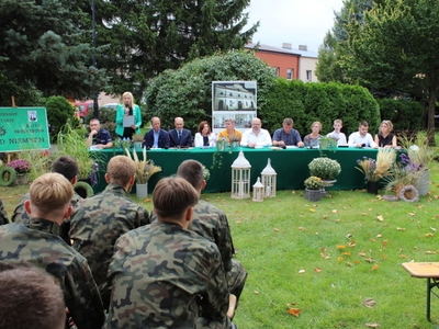 Zdjęcie wykonane w parku na Placu Wolności w Sompolnie. Przedstawia stół za którym siedzą lektorzy Narodowego Czytania. Z lewej strony plakat „Nad Niemnem” Eliza Orzeszkowa oraz Pani Katarzyna Janicka czytająca powitanie.