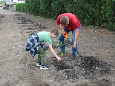 Zdjęcie przedstawia chłopca sadzącego swoje drzewo oraz burmistrza zakopującego korzenie tego drzewa.