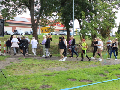 Zdjęcie przedstawia miejsce startu marszu z kijami. Widać grupę osób wyruszających na marsz.