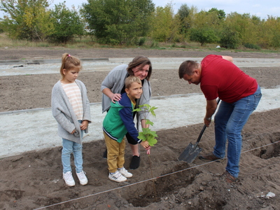 Fotografia prezentuje kobietę z dziećmi oraz burmistrza, który sadzi drzewo.