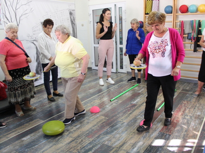 Zdjęcie przedstawia salę rehabilitacyjną Domu Dziennego Pobytu na której odbywa się zadanie sprawnościowe – tor przeszkód z jabłkiem na rakietce do badmintona.
