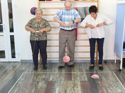 Fotografia ukazuje jednego mężczyznę i dwie kobiety podczas nawijania na rolkę sznurka z jabłkiem przymocowanym na końcu.