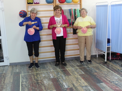 Zdjęcie przedstawia trzy seniorki podczas wyścigu nawijania na rolkę sznurka z przymocowanym na końcu jabłkiem.