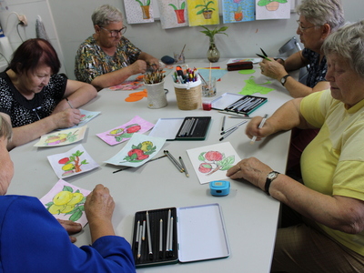 Zajęcia w pracowni plastycznej podczas których grupa seniorek maluje akwarelowe obrazki, których tematem są jabłka.