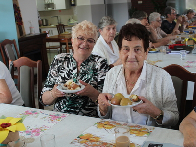 Fotografia prezentuje dwie kobiety pozujące do zdjęcia z pieczonymi jabłkami na talerzu.