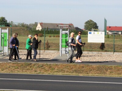 Zdjęcie przedstawia kobiety spacerujące z kijkami do Nordic Walking. W tle siłownia plenerowa.
