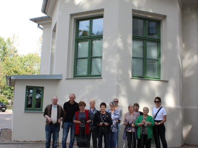 Zdjęcie przedstawia grupę seniorów wraz z opiekunami na tle pałacu we Wierzbinku.