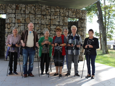 Fotografia ukazuje pięć kobiet i jednego mężczyznę stojących na scenie plenerowej w parku we Wierzbinku. W tle ściana z kamieni.