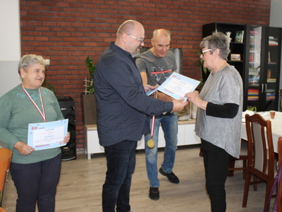 Na pierwszym planie dyrektor MGOPS wręcza laureatce medal i dyplom. W tle mężczyzna, a z lewej strony starsza kobieta z medalem i dyplomem.