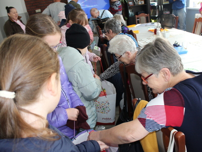 Zdjęcie przedstawia dzieci częstujące seniorów herbatami.
