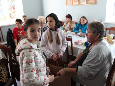 Na zdjęciu seniorka wybierająca herbatę z torebki w tle inni seniorzy
