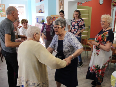 Zdjęcie przedstawia seniorów wraz z opiekunami tańczących na sali głównej DDP.