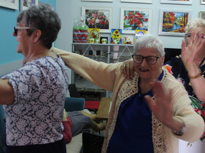 Fotografia przedstawia seniorów w sali wypoczynkowej tańczących do piosenki „Jedzie pociąg z daleka”.