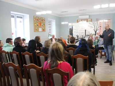 Zdjęcie przedstawia wnętrze sali głównej DDP .Na pierwszym planie widać Dyrektora MGOPS przemawiającego do publiczności.