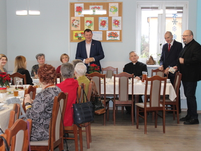 1)	Zdjęcie wykonane w sali głównej Domu Dziennego Pobytu dla Osób Starszych w Sompolnie. Przedstawia zaproszonych gości oraz seniorów obecnych na spotkaniu wigilijnym.