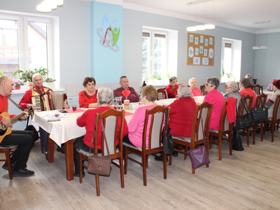 Zdjęcie wykonane w sali głównej Domu Dziennego Pobytu podczas balu karnawałowego. Widać na nim seniorów siedzących przy stole.