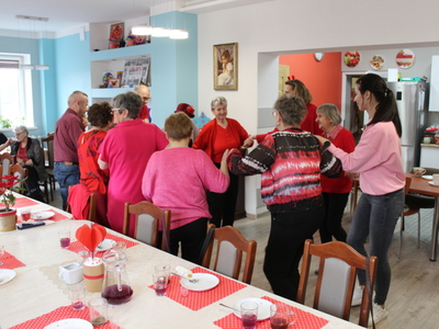 Zdjęcie przedstawia seniorów wraz z opiekunami tańczących w kółku.